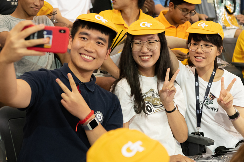 Three first-year students wearing RAT caps take a selfie during Convocation.