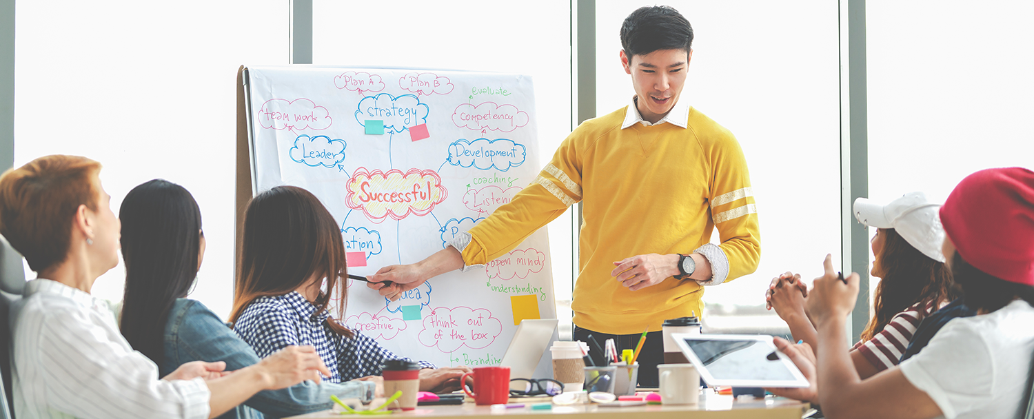 Asian young man presenting to a group. On the presentation flip board leadership related words are displayed.