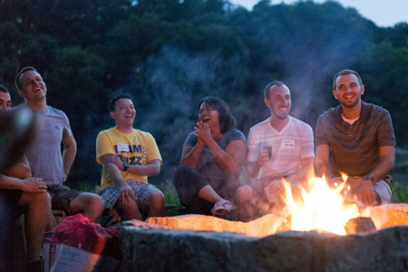 A group of people laughing in front of a campfire.