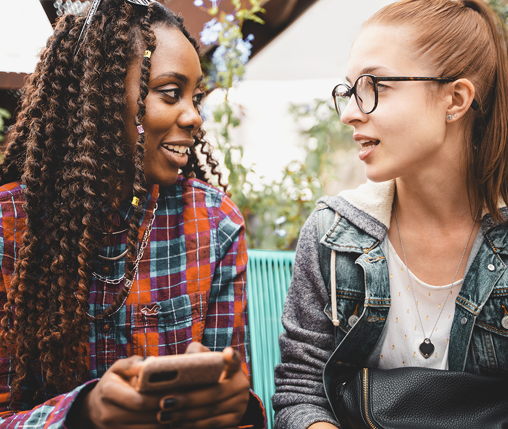 Two young woman talking. One is Black and the other white.